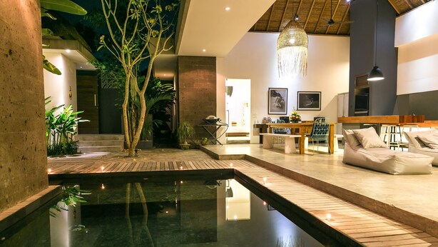 A modern interior with a central water feature, wooden flooring, and a seating area with cushions. - Villa Turtle (Seminyak)