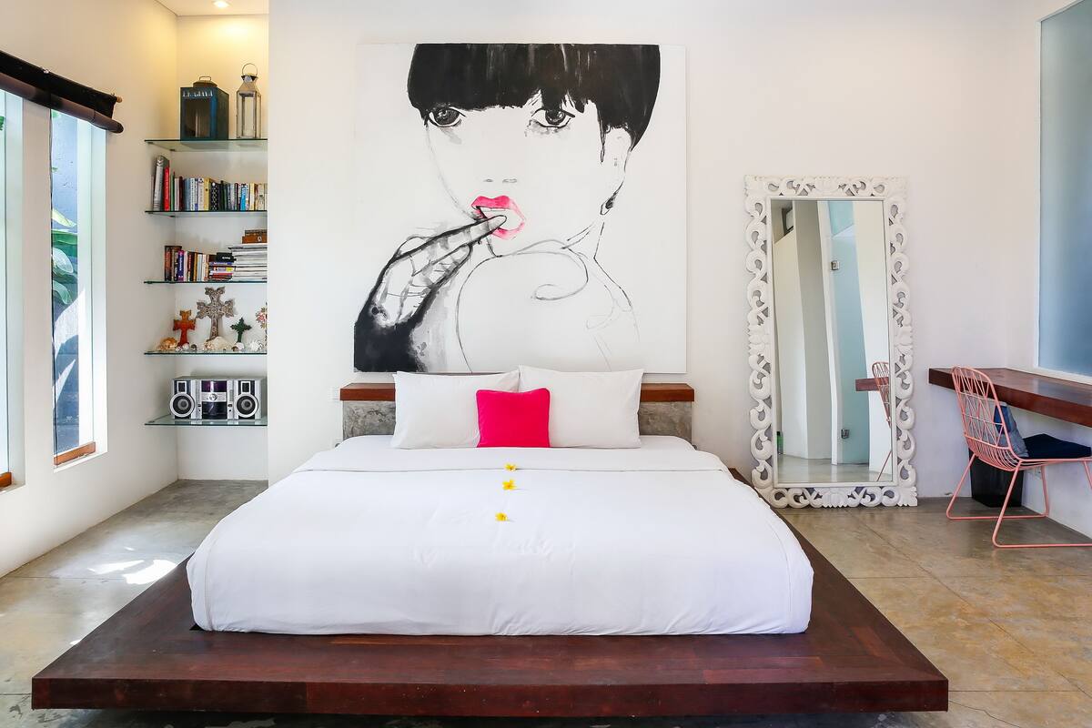 A modern bedroom with a large bed, a bookshelf, a mirror, and a desk.