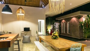 A modern dining area with a wooden table, bar stools, and hanging light fixtures. - Villa Turtle (Seminyak)