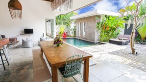 A modern outdoor dining area with a pool, surrounded by lush greenery and a clear blue sky. - Villa Turtle (Seminyak)