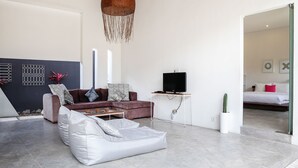 A modern living room with a sofa, a white pouf, a TV on a stand, and a cactus plant. - Villa Turtle (Seminyak)