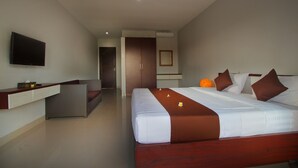 A modern hotel room with a large bed, a flat-screen TV, a seating area, and a bathroom. - Sri Kandi Inn (Kedonganan)