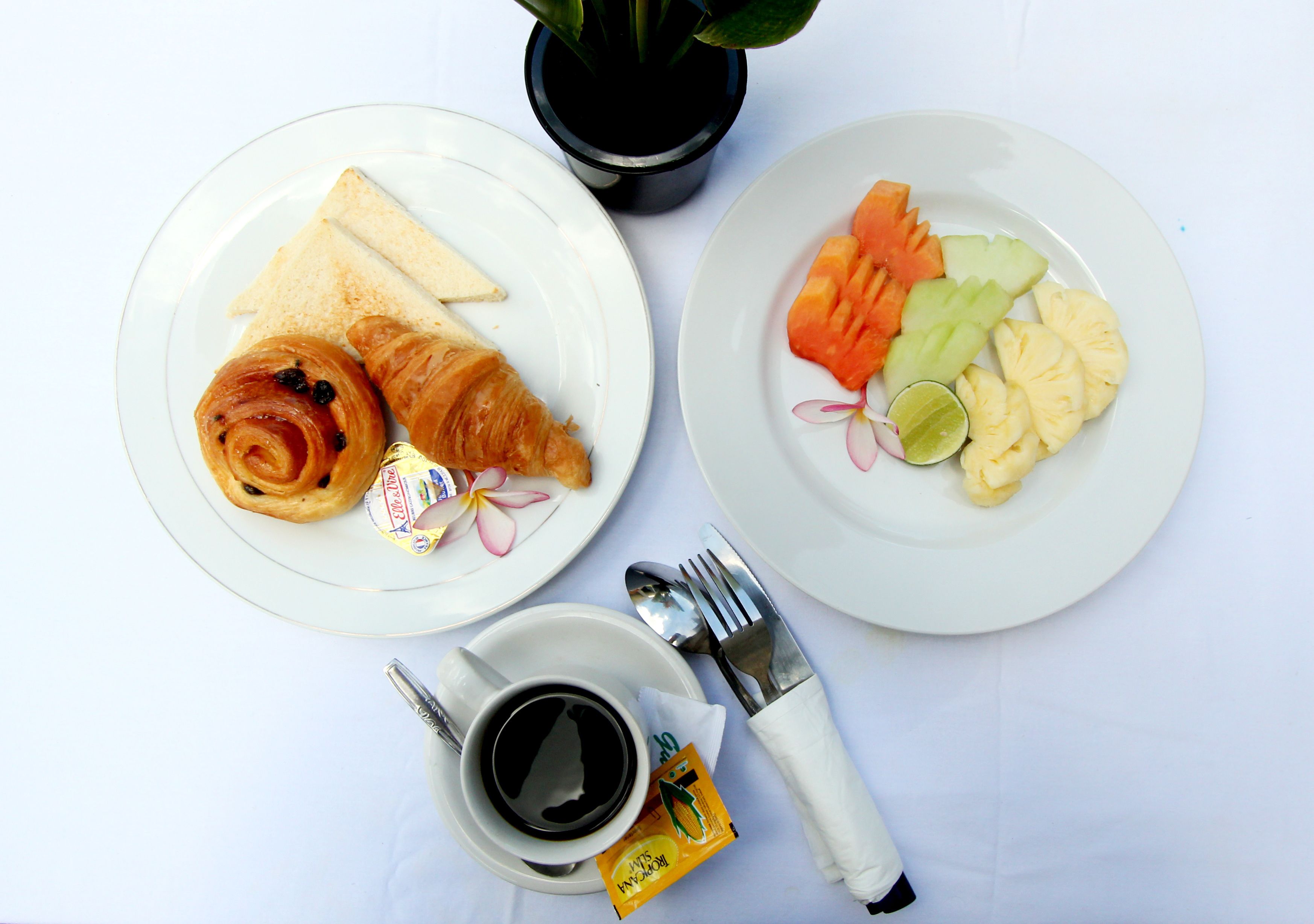 Deux assiettes de nourriture, une tasse de café, une fourchette et une cuillère, le tout posé sur une nappe blanche.