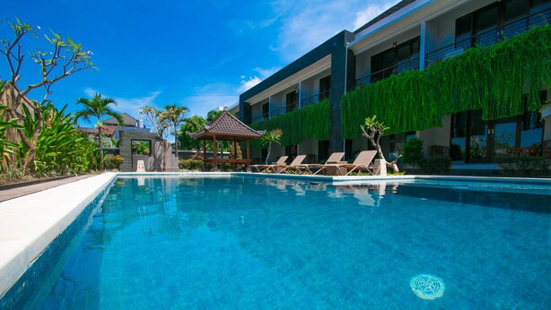 A clear blue pool with lounge chairs and a gazebo, surrounded by greenery and modern buildings. - Sri Kandi Inn (Kedonganan)
