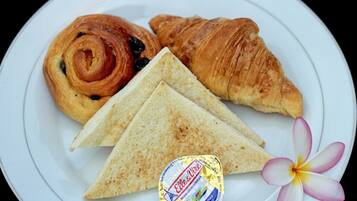 A plate with a croissant, a swirl pastry, and two slices of bread, accompanied by a flower and a butter packet.