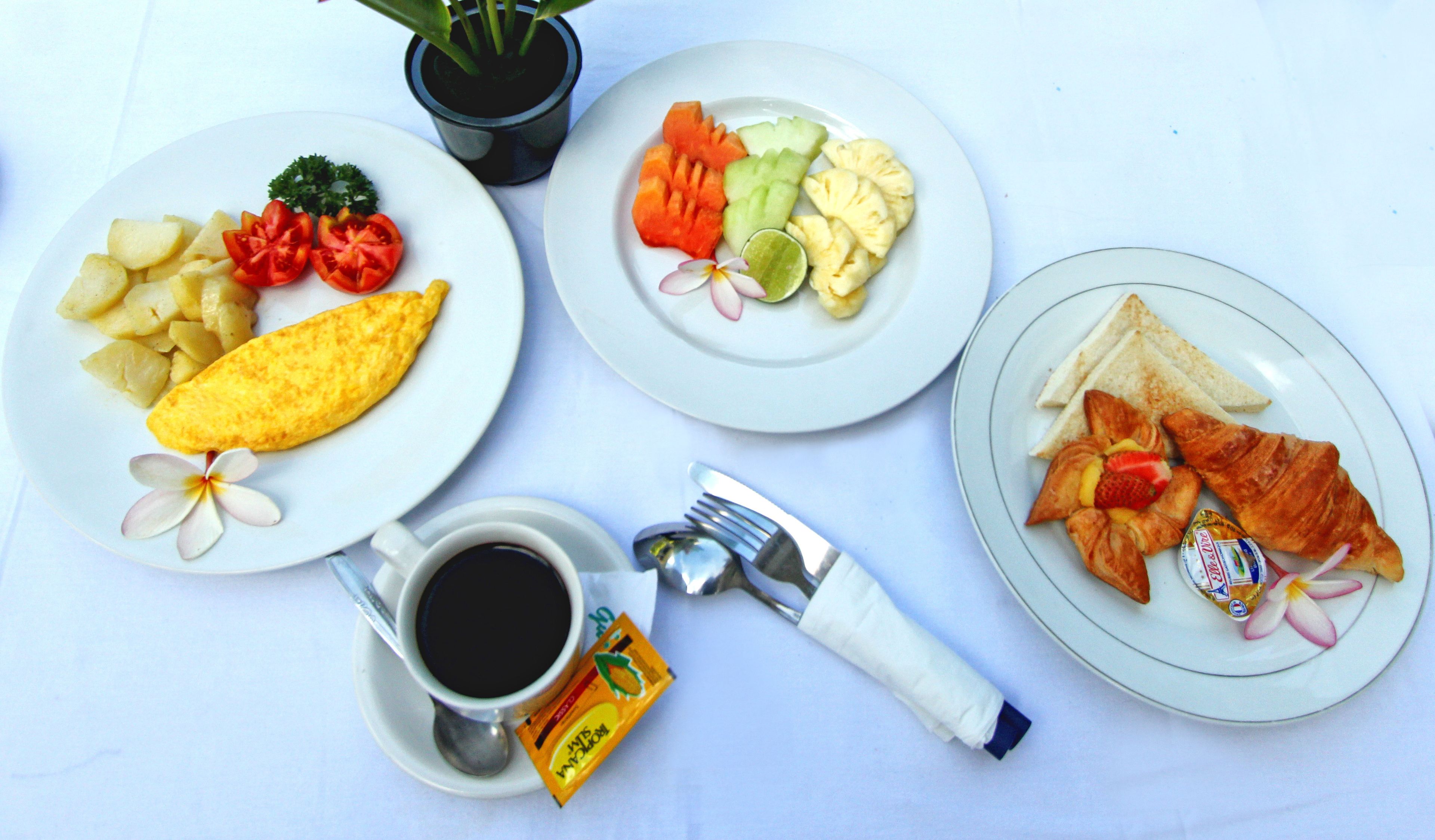 A table with plates of food, a cup of coffee, a plant, and a napkin.
