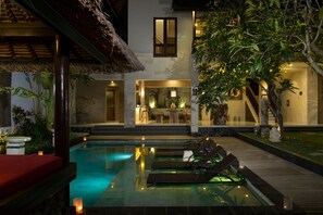 A pool area with lounge chairs, a dining area, and a staircase leading to a second floor. - The Secret Villas (Seminyak)