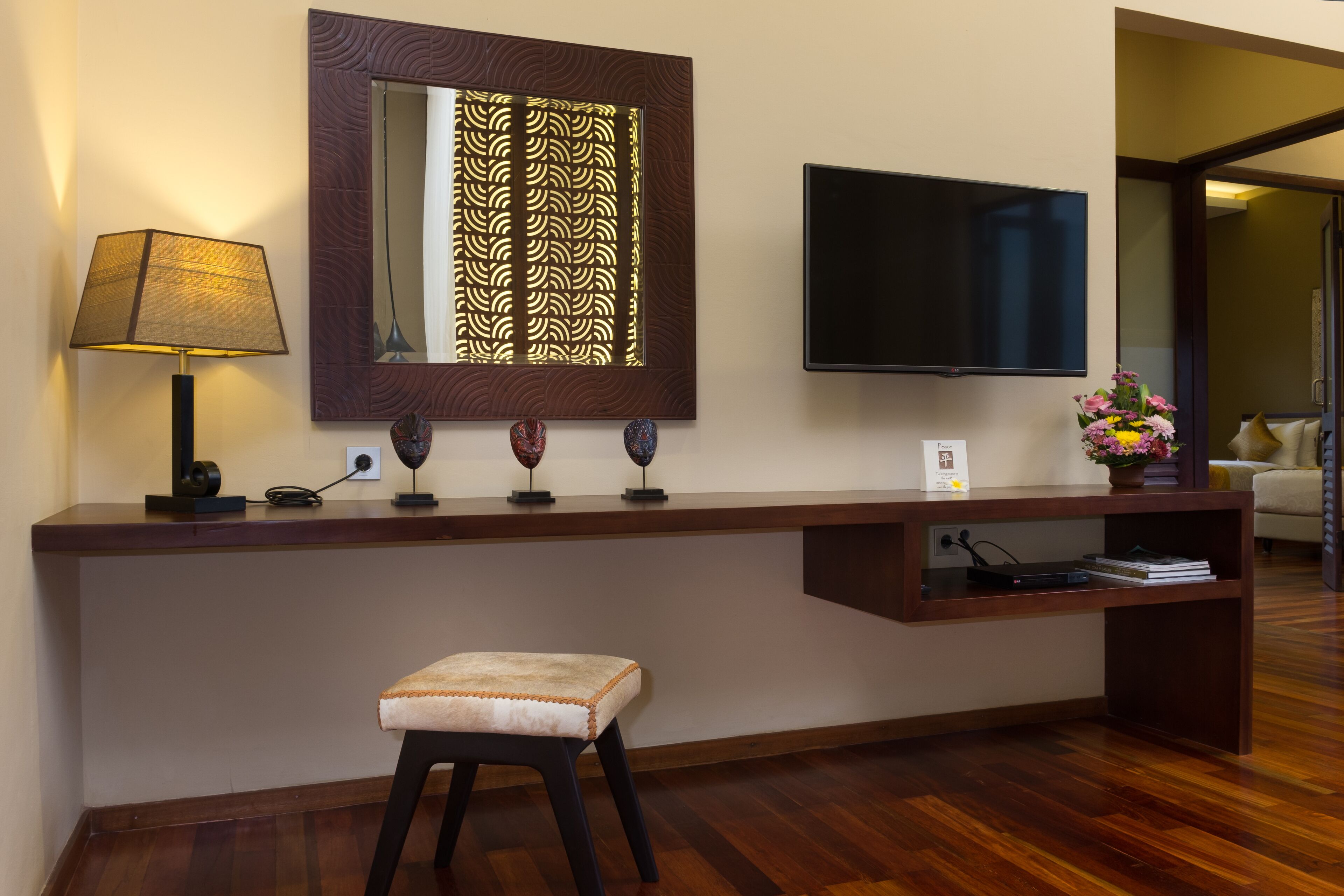 A hotel reception desk with a flat-screen TV, a lamp, decorative items, and a small stool.