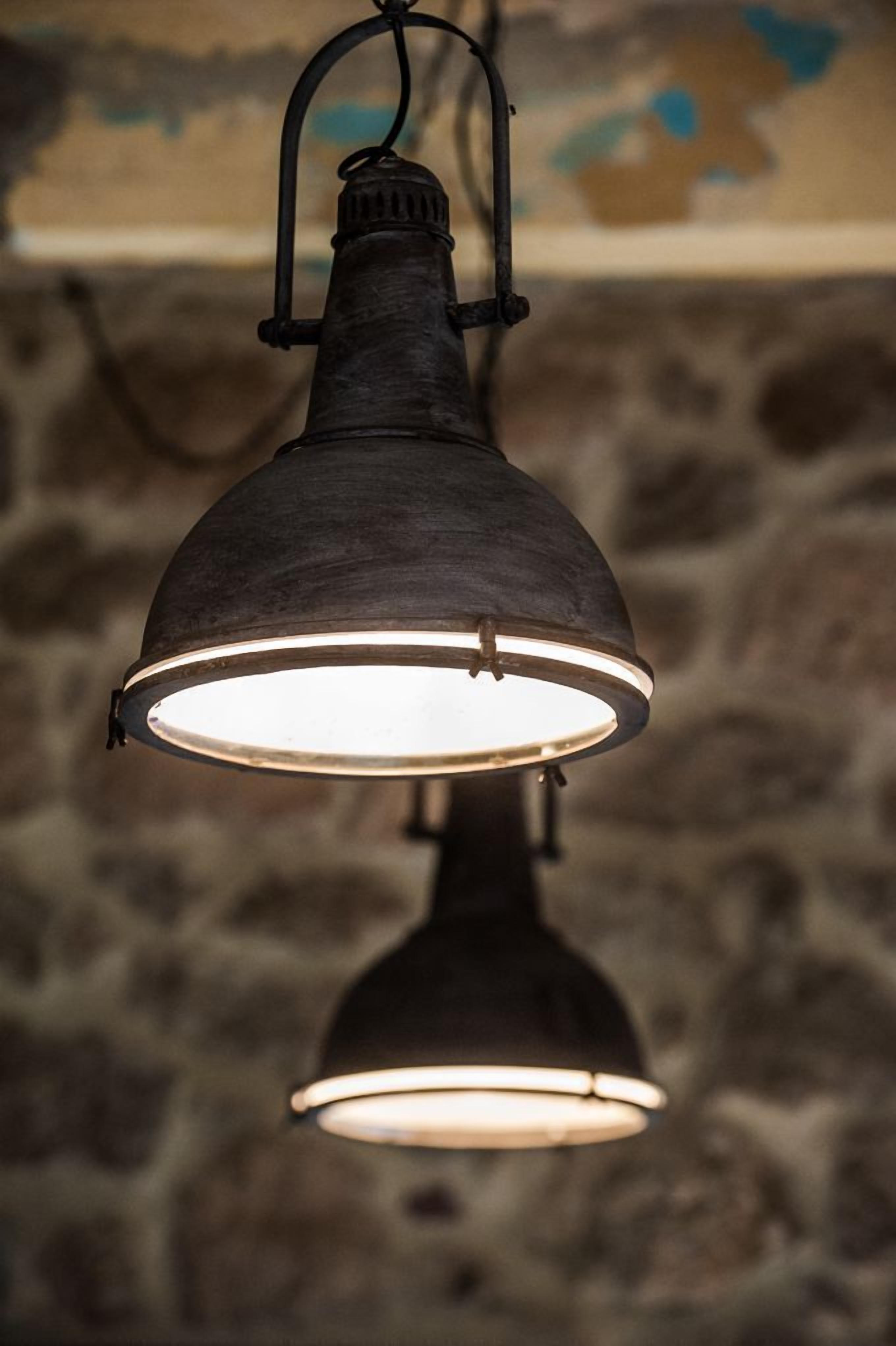 Una lámpara colgante con detalles metálicos, suspendida sobre un techo con pared de piedra.
