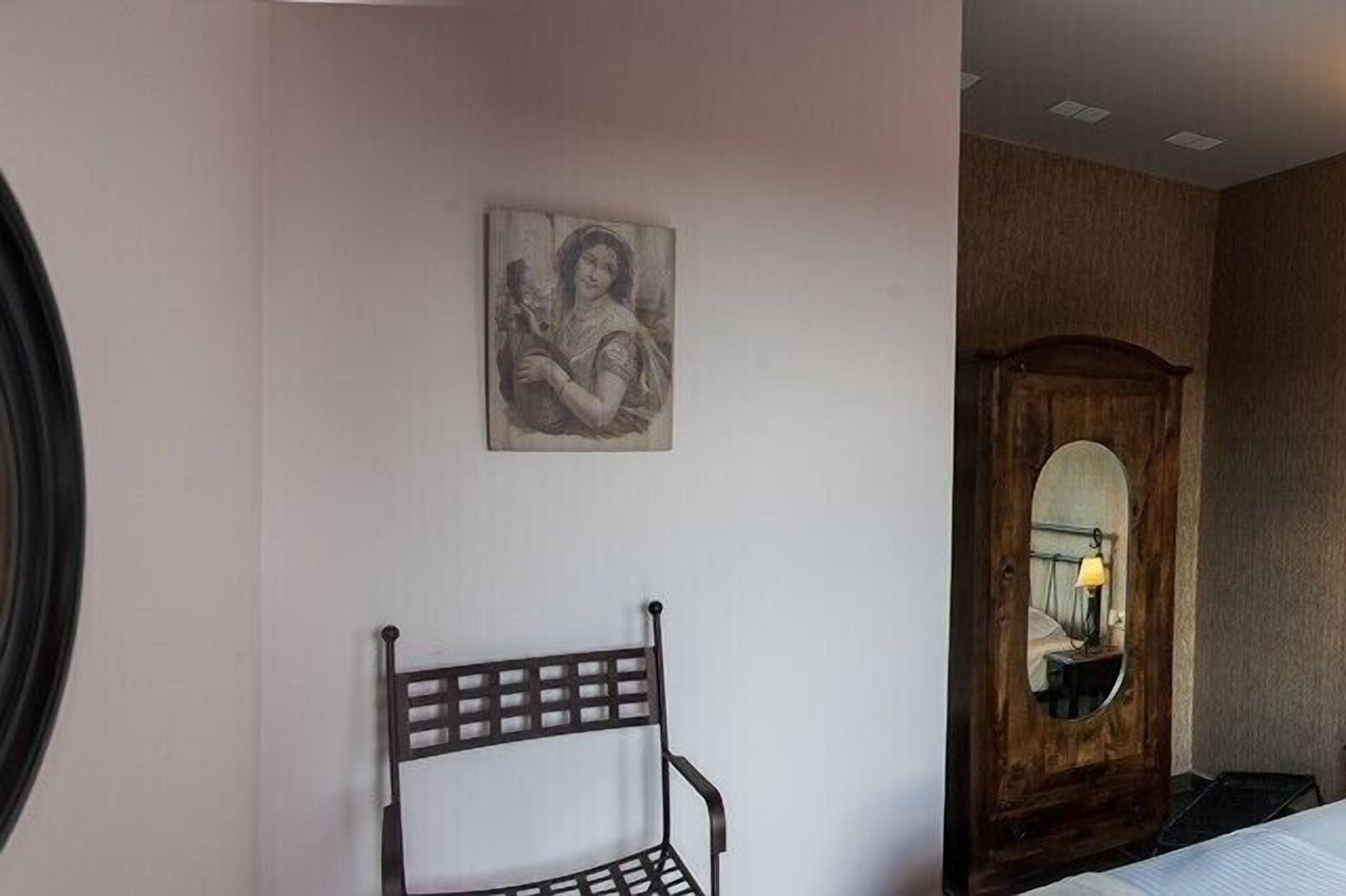 A room with a bed, a wooden wardrobe, a wall-mounted mirror, and a framed picture.