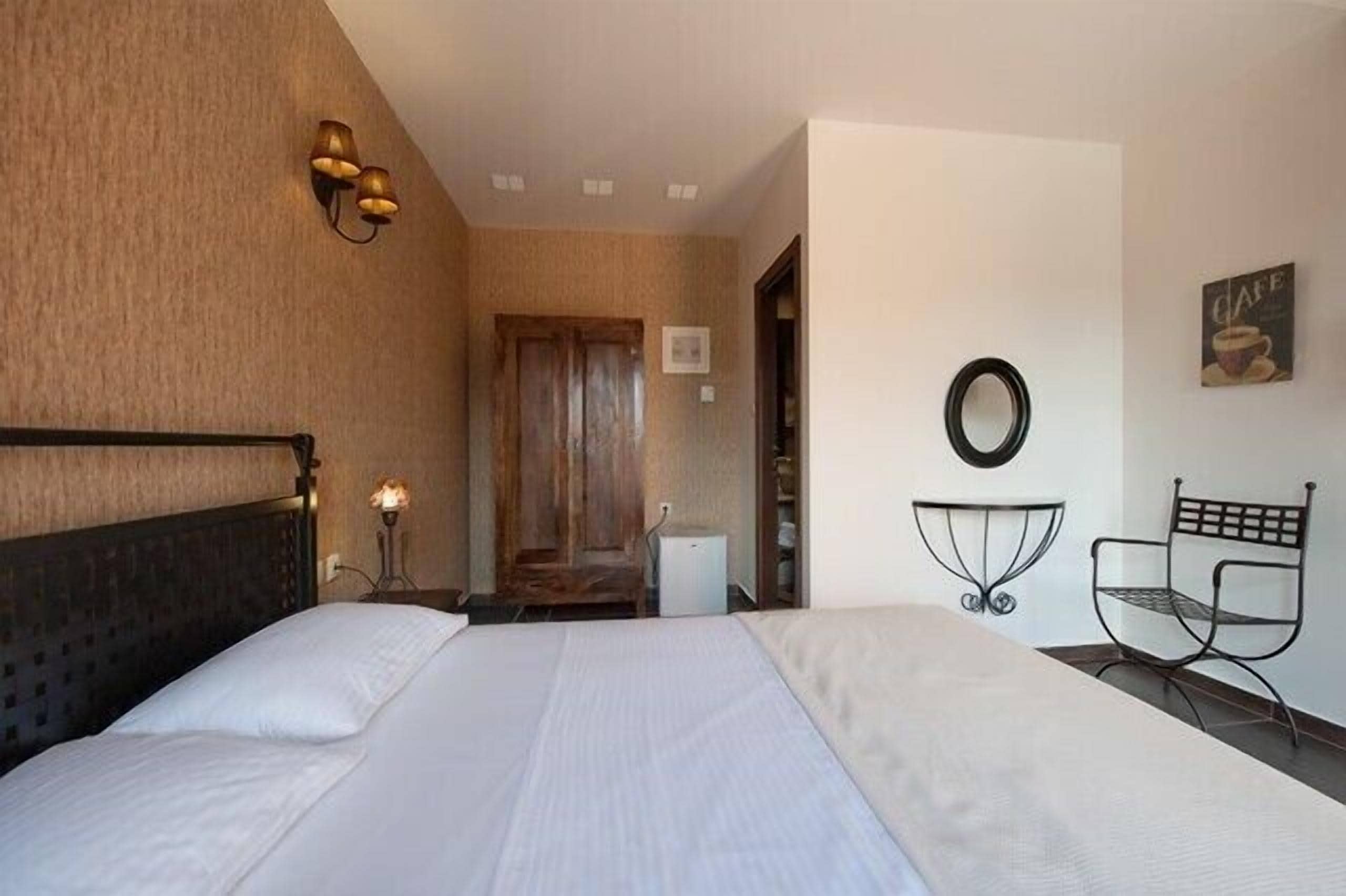 Habitación de hotel con una cama grande, una lámpara de noche, una mesita, una silla y un espejo instalado en la pared.