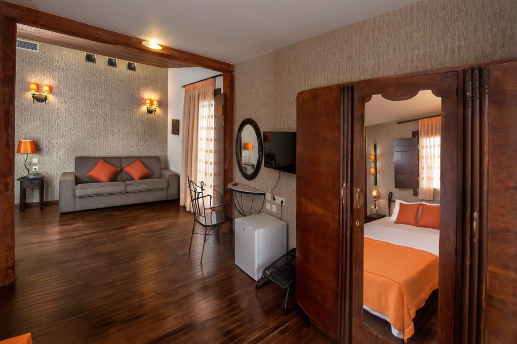 Quarto de hotel com sofá, cama, mesa pequena, cadeira, televisão e espelho.