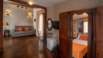 Quarto de hotel com sofá, cama, mesa pequena, cadeira, televisão e espelho.