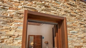 A room with a stone wall, a wooden door, a bed, and a wall-mounted light fixture. - Polys Guest House (Pydna-Kolindros)