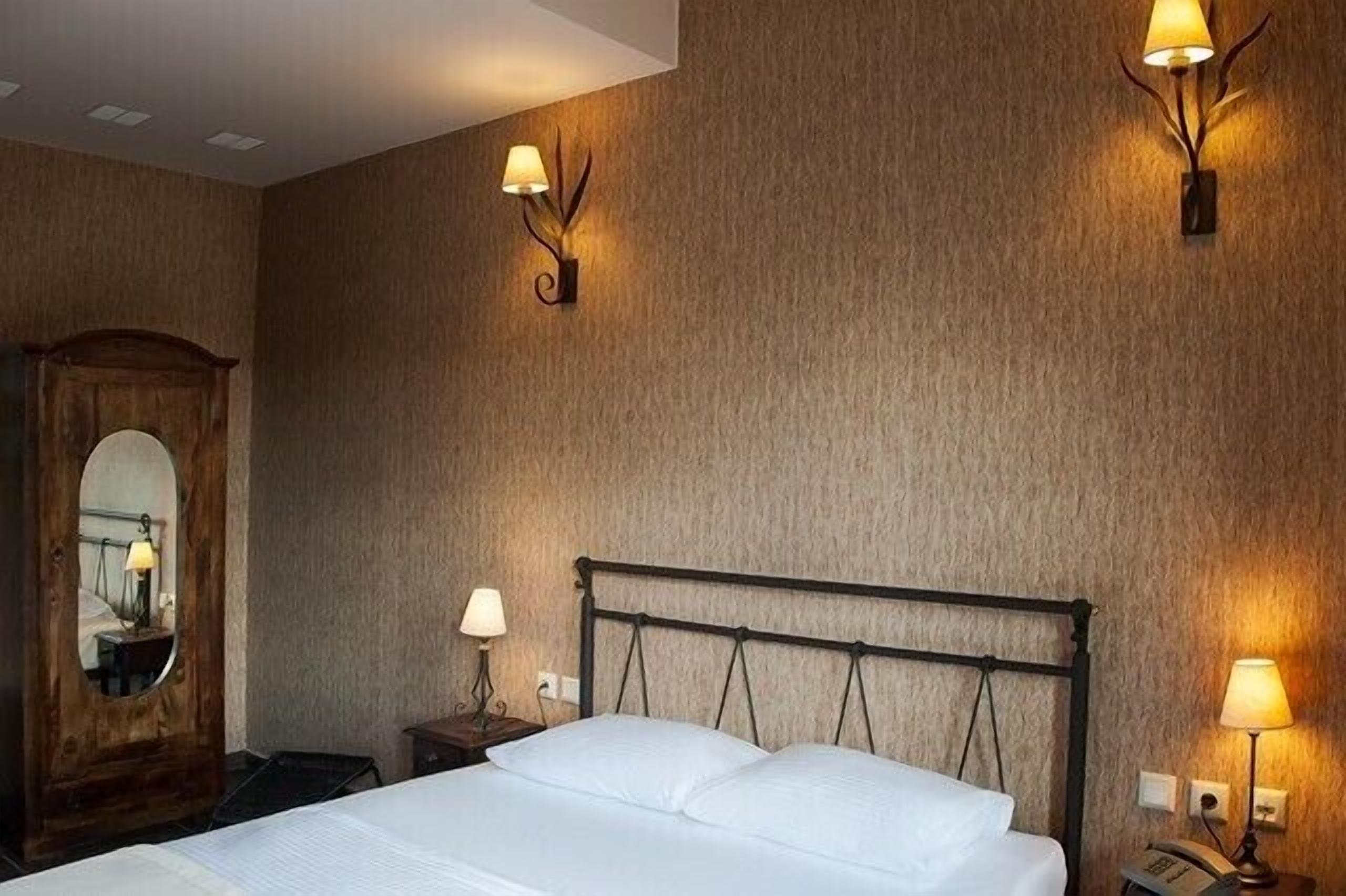 Ein Hotelzimmer mit einem Bett, zwei Nachttischlampen, einem Spiegel und einer Wandleuchte.