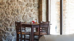 A stone wall interior with a table and chairs, a hanging light fixture, and a large window. - Polys Guest House (Pydna-Kolindros)