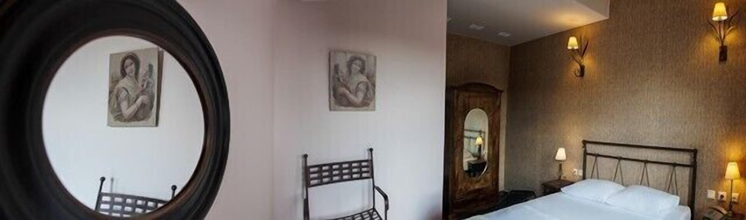 Habitación de hotel con cama, mesita de noche, espejo y dos sillas.