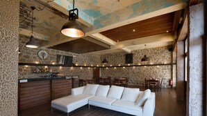 A spacious living area with a large white sectional sofa, a stone accent wall, and a rustic wooden ceiling. - Polys Guest House (Pydna-Kolindros)