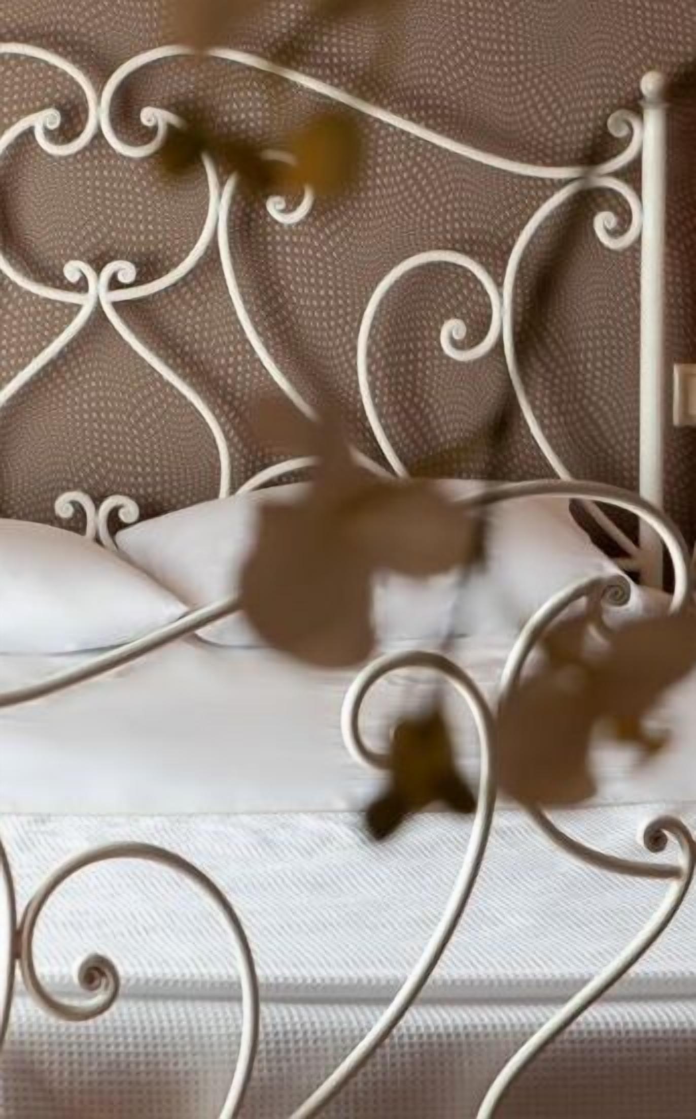 Una cama con estructura metálica blanca y cabecera de tela con textura.