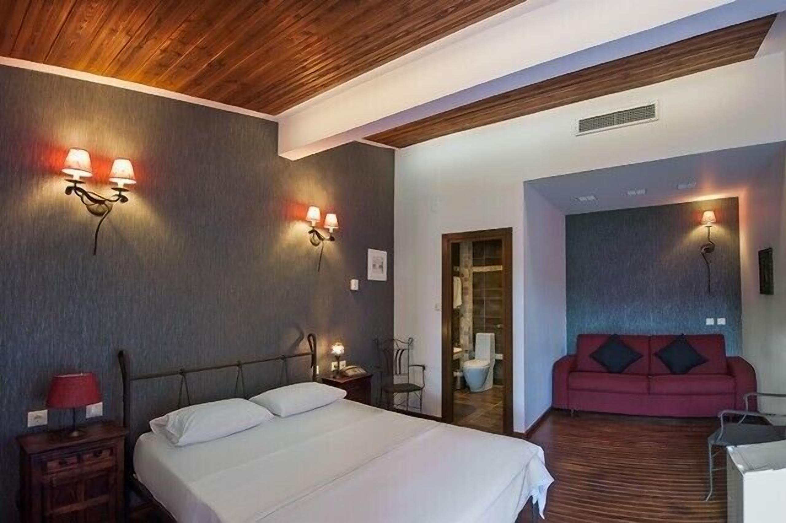 Habitació d'hotel amb un llit, un sofà vermell i làmpades penjades a la paret.