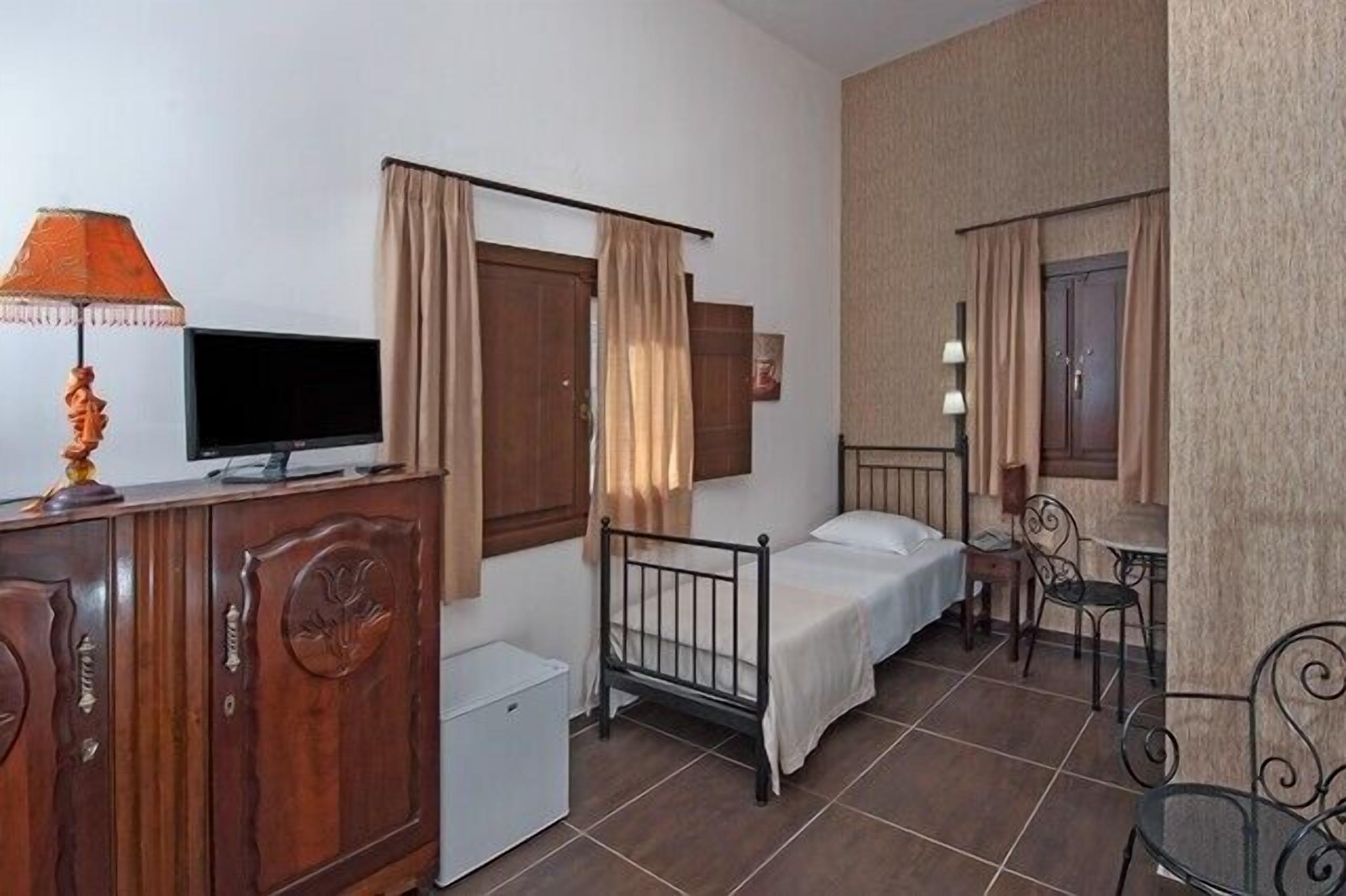 A small, neatly arranged bedroom with a single bed, a desk, and a television on a wooden cabinet.