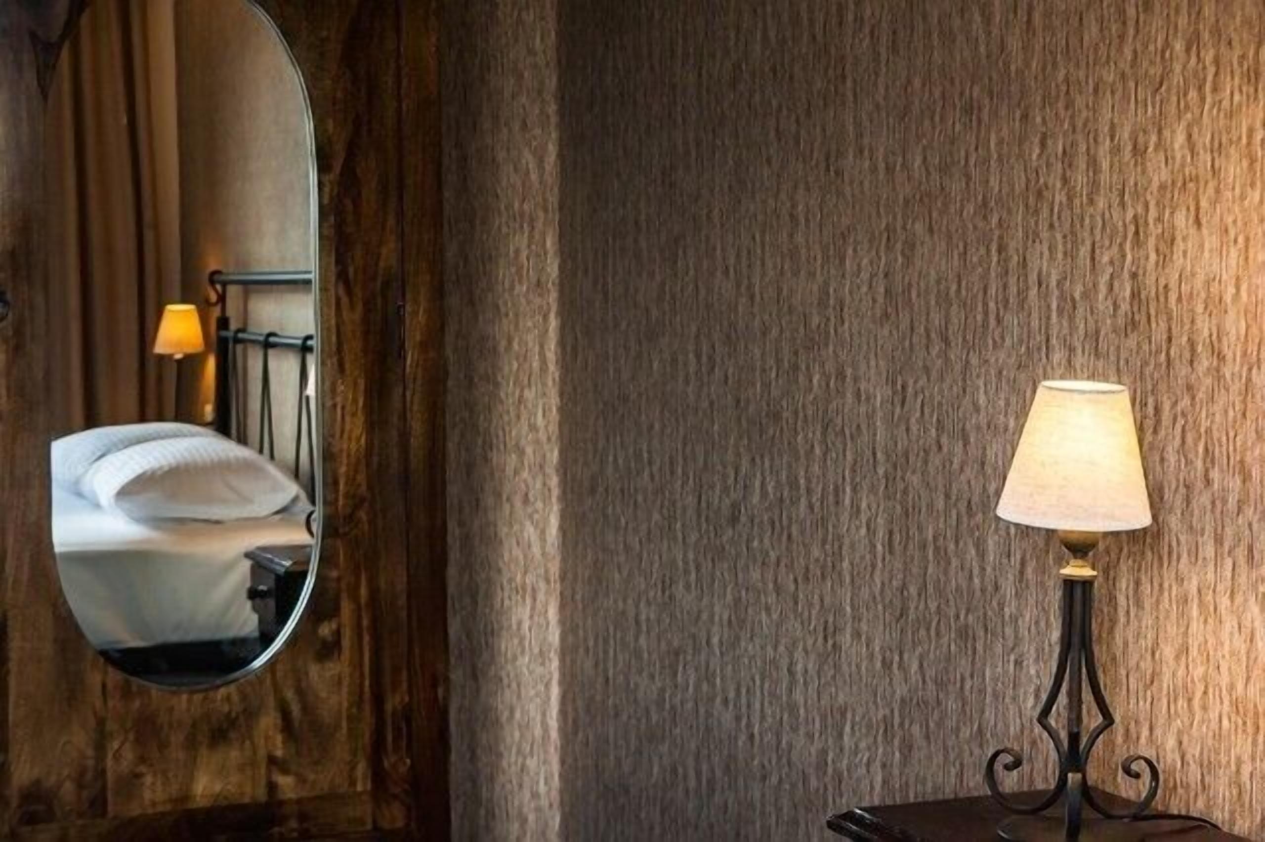Una habitación de hotel con pared de madera, un espejo redondo, una cama y una lámpara de mesa.