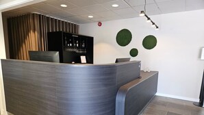 A reception area with a curved reception desk, a black shelving unit with glassware, and two green circular wall decorations. - Hotell Fritidsparken (Skien)