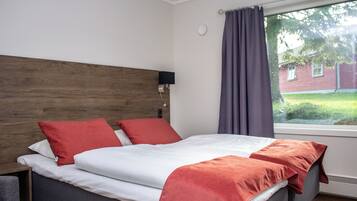 Ein Hotelzimmer mit Bett, Kopfteil, Fenster mit Vorhängen und Blick auf ein Gebäude.