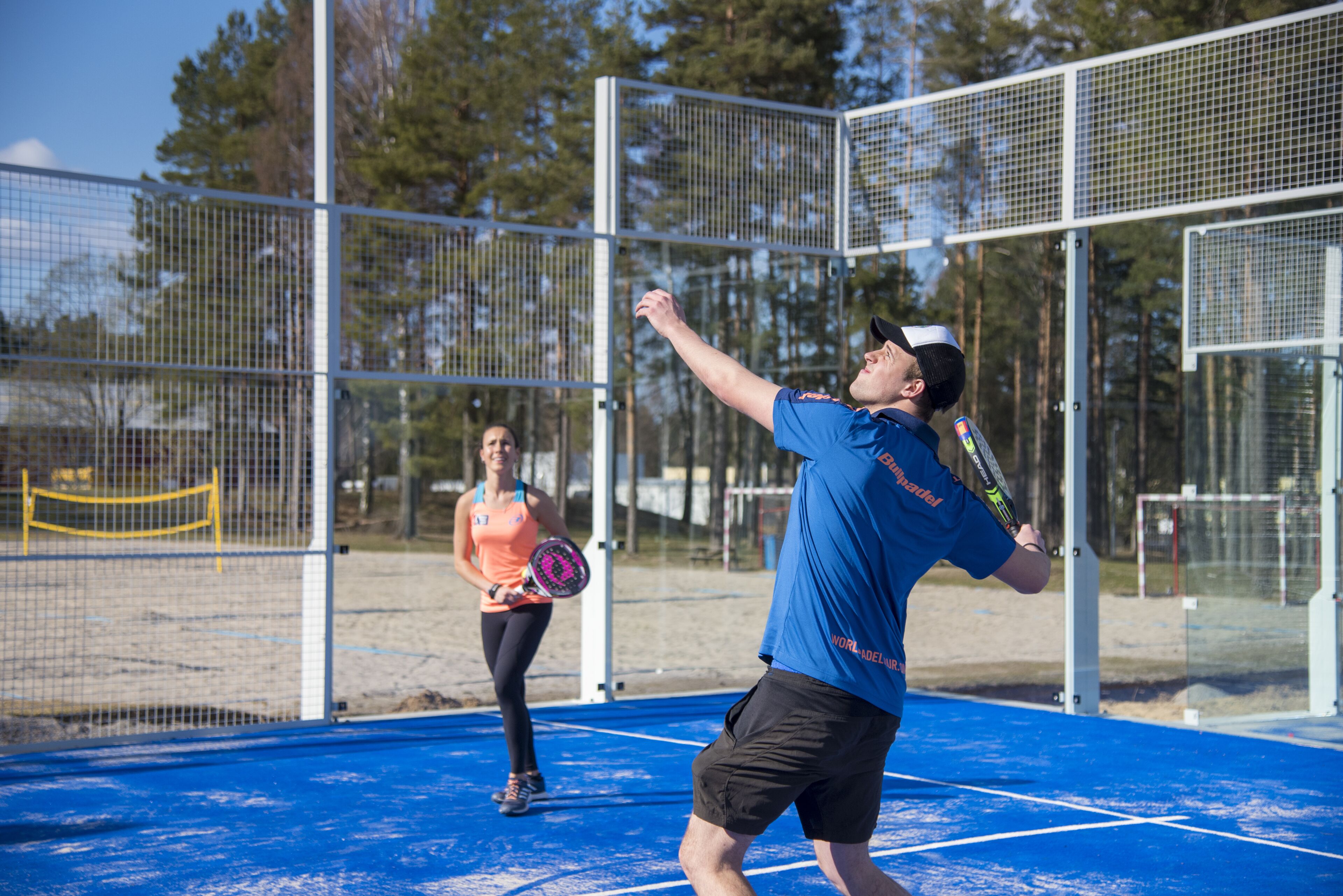 Una cancha de tenis con una red, un jugador con camisa azul y una pelota en el aire.