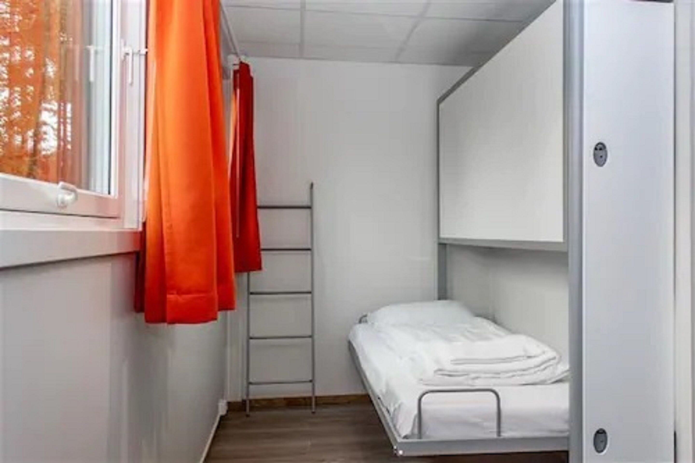 Ett litet rum med en våningssäng, en stege och ett fönster med orangea gardiner.