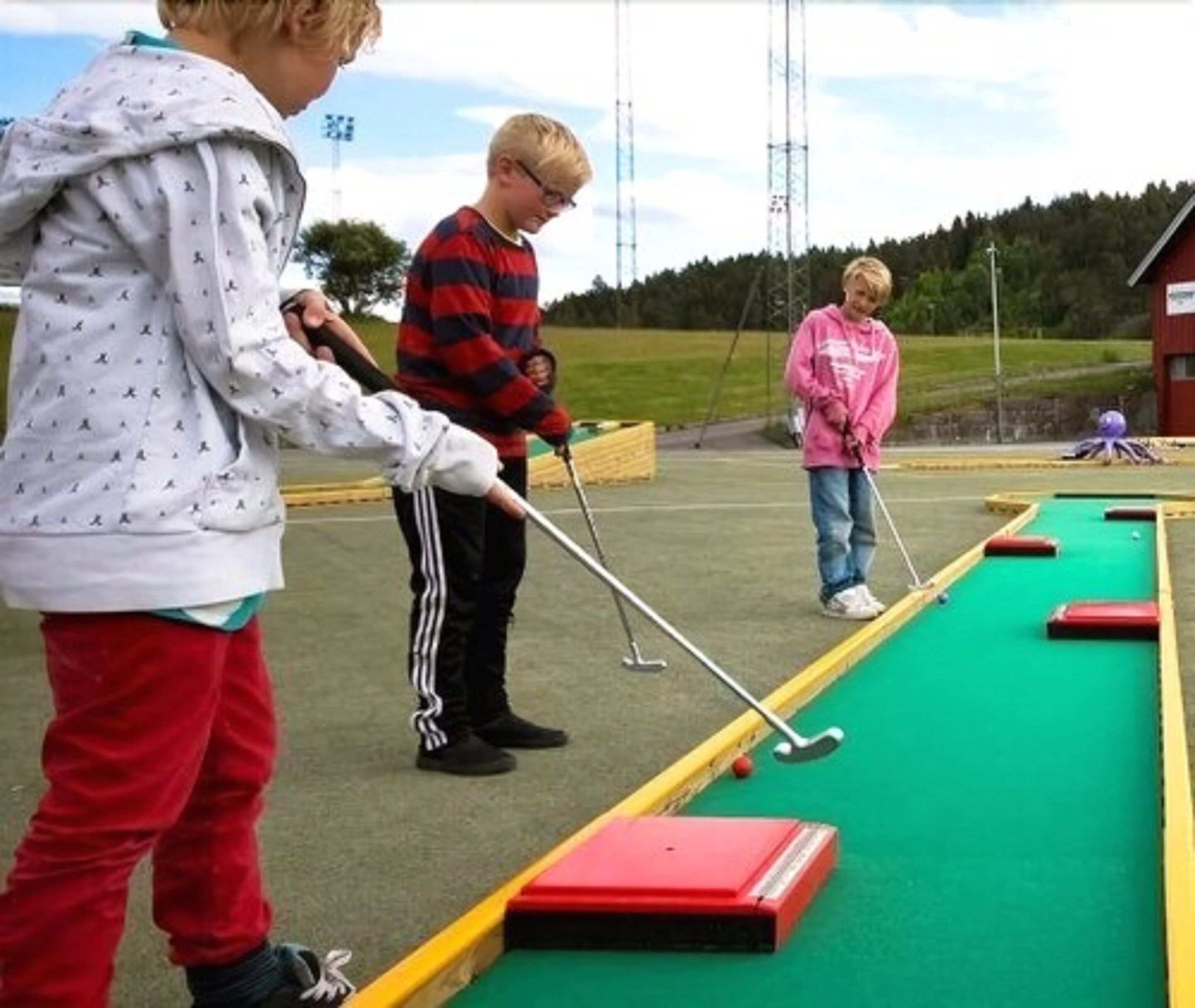 A group of people playing a lawn game, possibly croquet, on a green field with a red and yellow boundary.