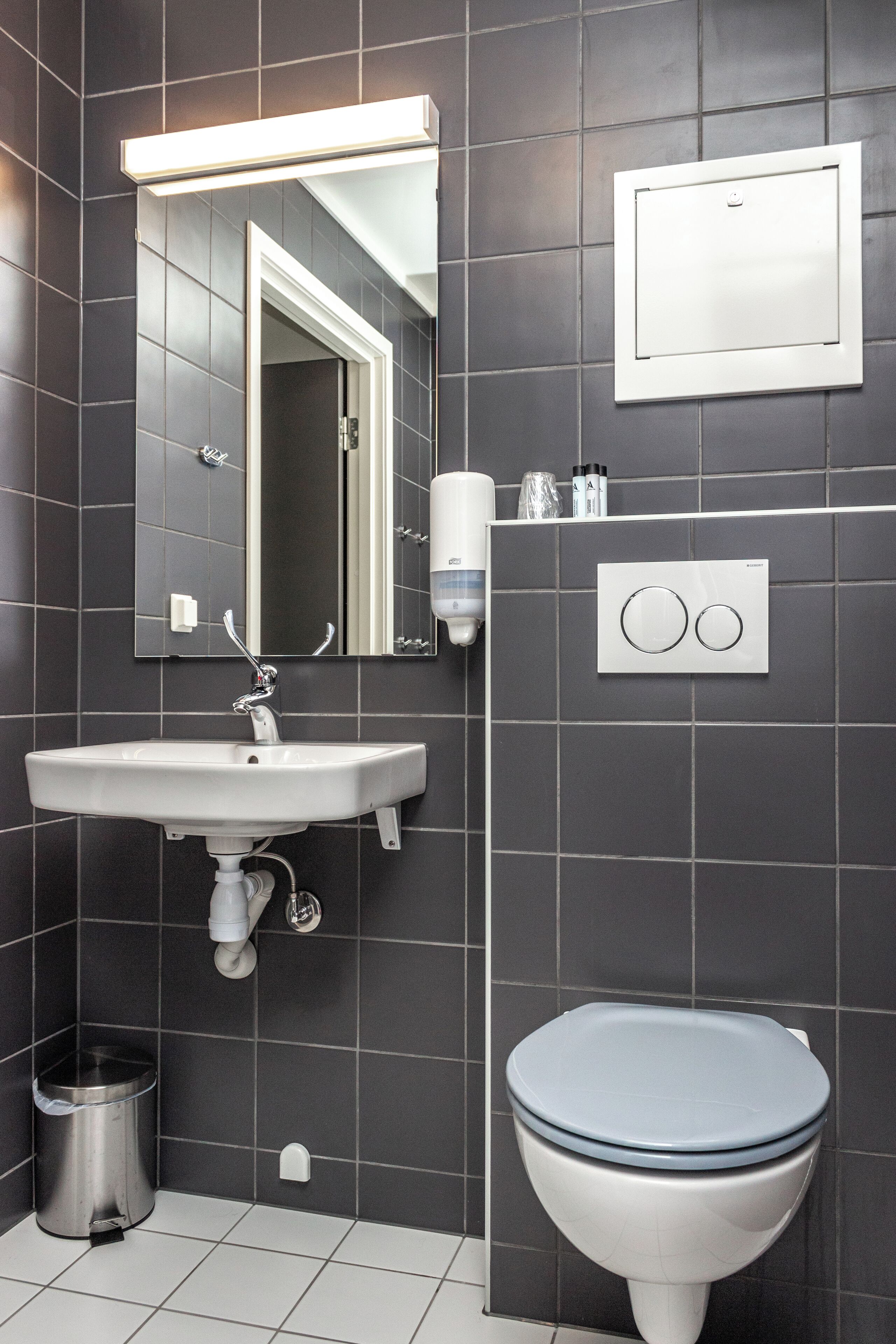 Un baño moderno con un lavamanos blanco, un espejo, un inodoro y un cubo de basura.