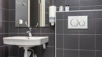 Un baño moderno con un lavamanos blanco, un espejo, un inodoro y un cubo de basura.