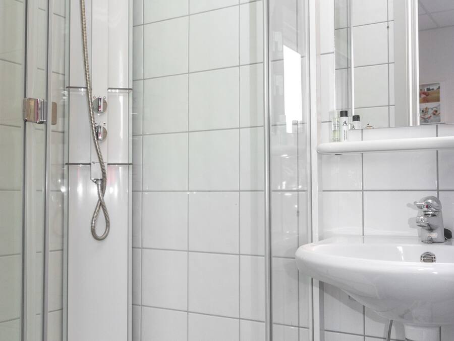Un baño moderno con ducha envuelta en vidrio, un lavamanos blanco y un espejo sobre él.