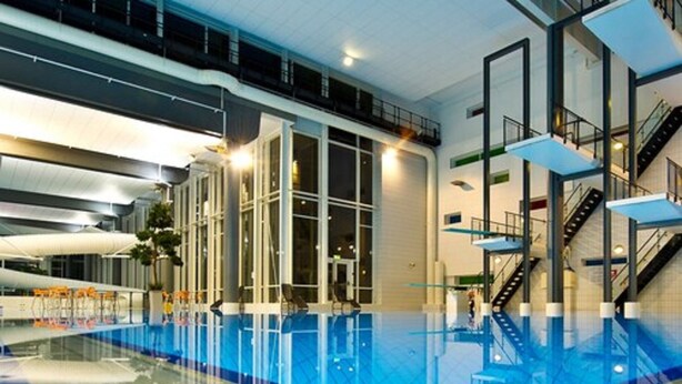 An indoor swimming pool with glass walls, a clear ceiling, and a modern architectural design. - Hotell Fritidsparken (Skien)