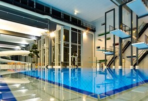 An indoor swimming pool with glass walls, a clear ceiling, and a modern architectural design. - Hotell Fritidsparken (Skien)