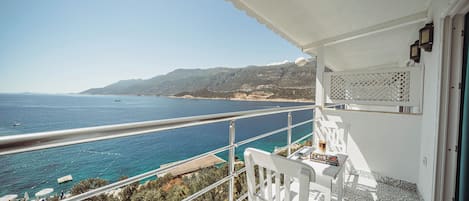 A balcony with a view of the sea, a white chair, and a table with a book and a glass.