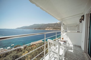 Un balcón con vista al mar, una silla blanca y una mesa con un libro y un vaso.