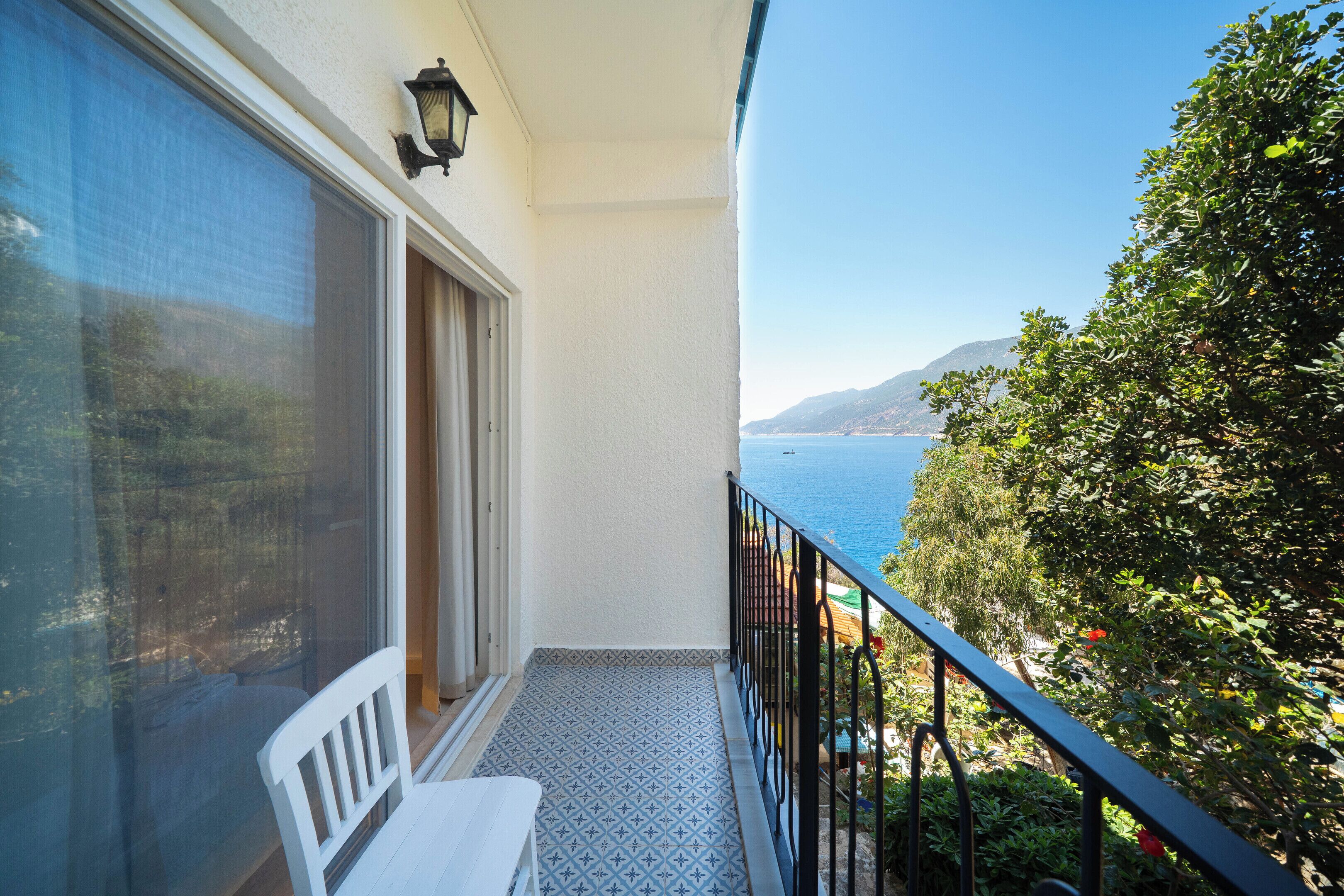 A balcony with a view of the sea, a white chair, and a patterned floor.