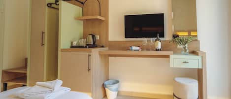 A hotel room with a bed, a desk with a TV, a mirror, a small stool, and a trash bin.
