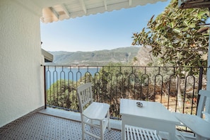 A balcony with a white chair, a small table, and a view of mountains and a body of water.