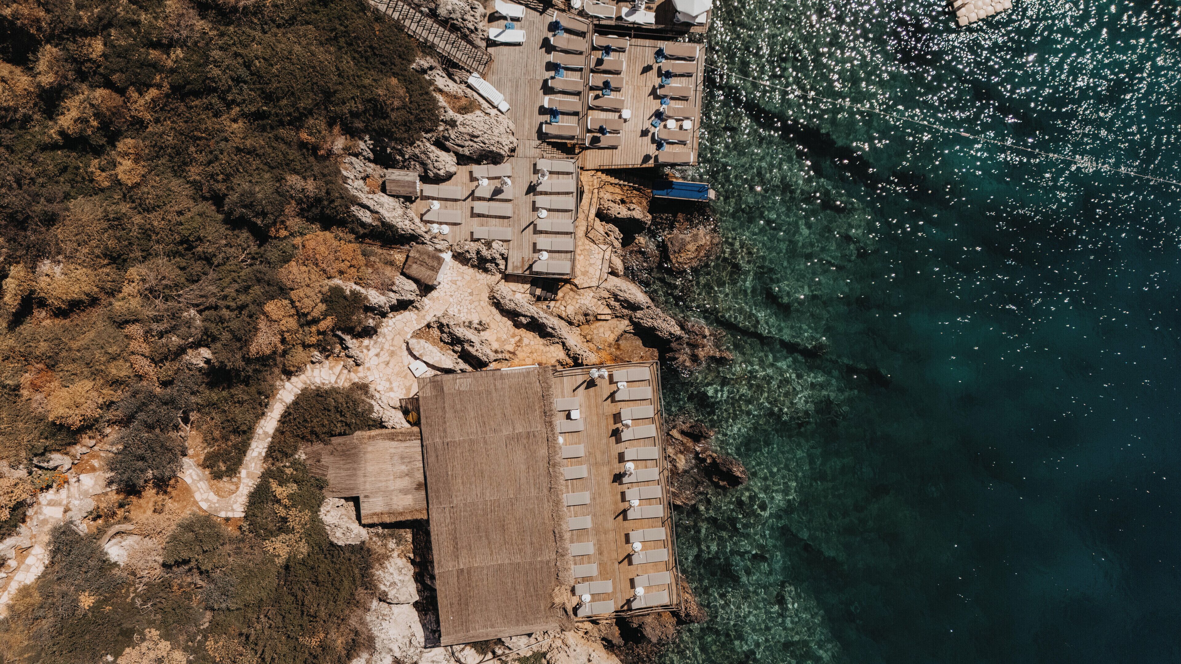 An aerial view of a coastal hotel with multiple sun loungers and a clear view of the ocean.