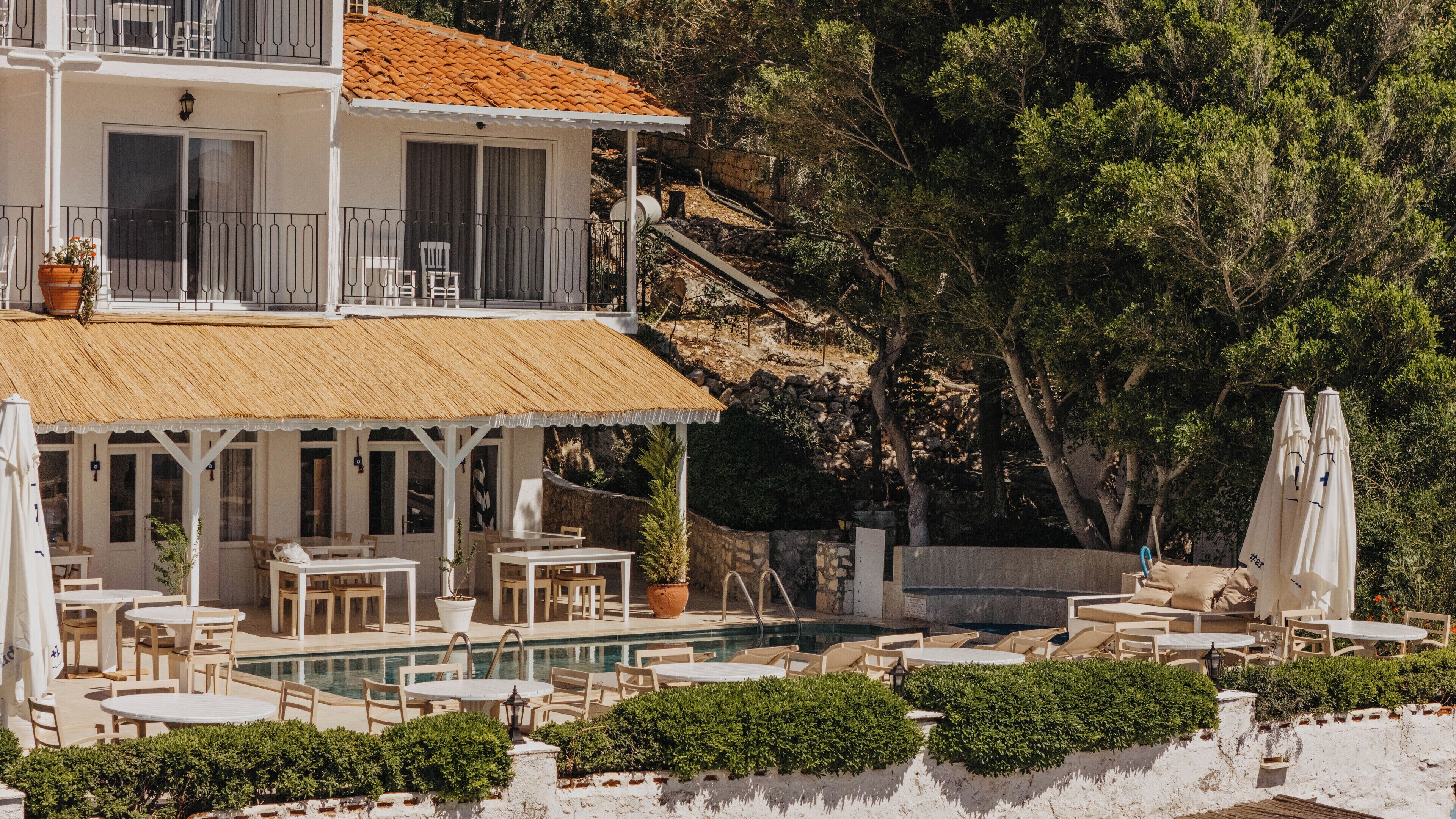 A two-story building with a pool area, outdoor seating, and a view of a rocky hillside.