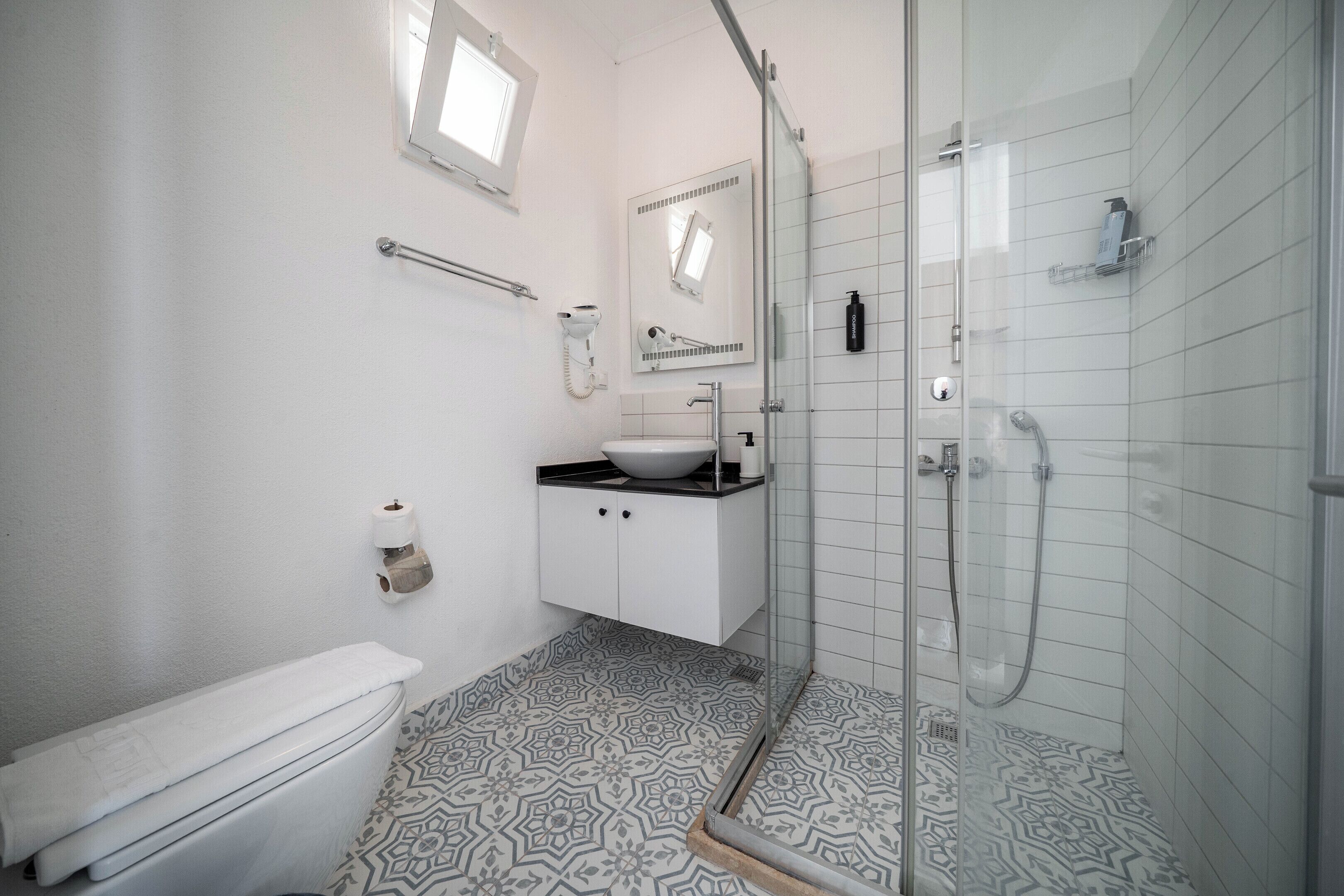 Un baño con inodoro, lavamanos, ducha y baldosas de suelo con diseño.