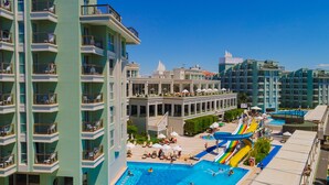 Un hôtel à plusieurs étages doté de balcons, d’un espace piscine avec toboggan et d’un coin salon extérieur.