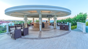 Un espace extérieur aménagé, abrité et doté de meubles en osier, avec un bar central, offrant une vue panoramique.
