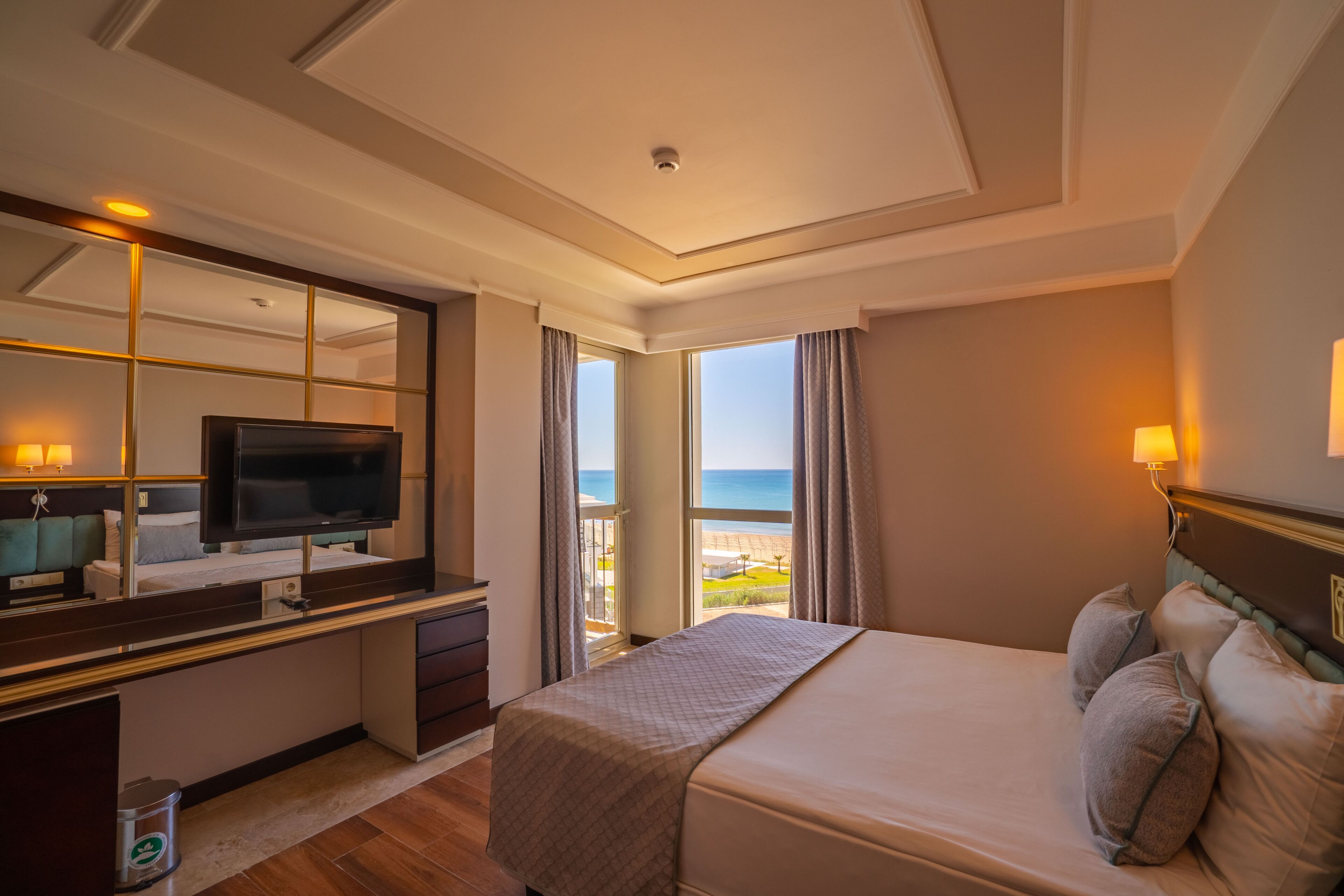 A hotel room with a bed, a TV, a desk, and a view of the ocean.