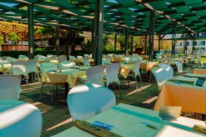 An outdoor dining area with tables and chairs, covered by a green roof structure. - Royal Atlantis Spa & Resort (Manavgat)