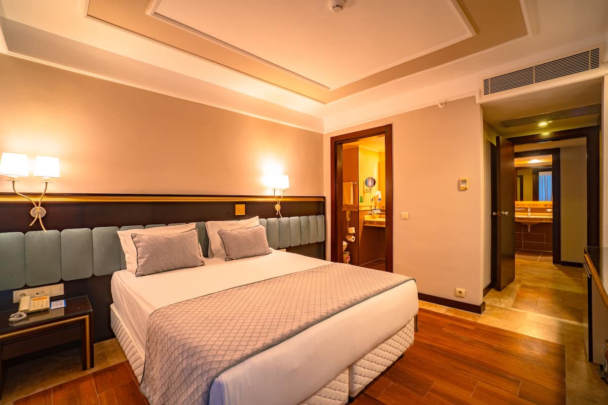 A hotel room with a large bed, bedside lamps, a nightstand, and a wooden floor.
