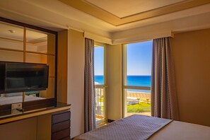 A hotel room with a bed, a TV, a desk, and a large window offering a view of the beach and ocean. - Royal Atlantis Spa & Resort (Manavgat)